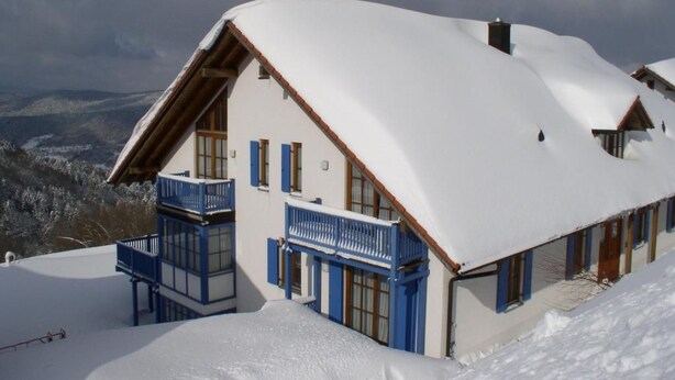 Een chalet bedekt met sneeuw, met een balkon, met bergen op de achtergrond.
