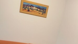 Een kamer met een oranje bank, een houten tafel met een kaars, en een gekaderd schilderij aan de muur.