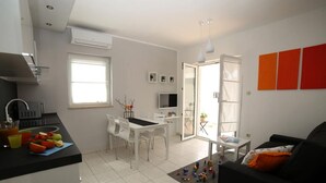 Un espacio habitable compacto con kitchenette, comedor y un sofá negro.