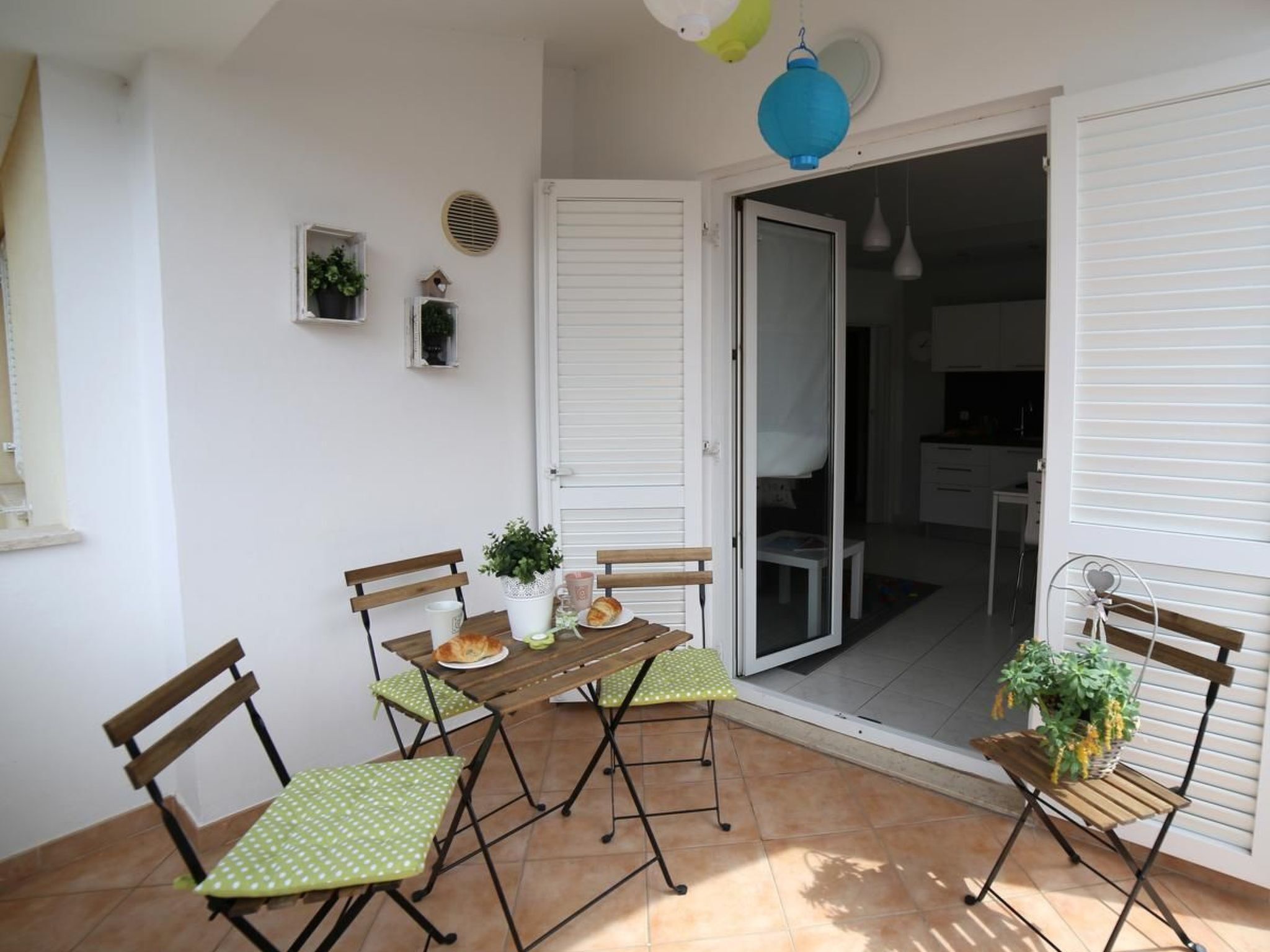 A dining area with a wooden table and chairs, a sliding glass door leading to a kitchen, and a small potted plant on a side table.