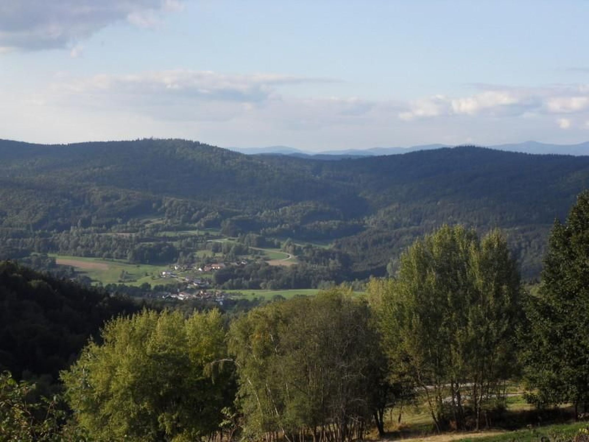 Ein weiter Blick über ein Tal mit einer kleinen Siedlung, umgeben von bewaldeten Hügeln.