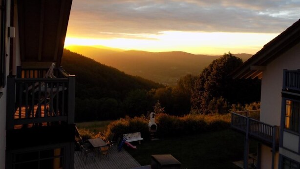 Un balcon donnant sur une vallée, avec une vue imprenable sur le coucher du soleil, une petite table et un banc.