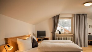 Ett mysigt hotellrum med en säng i trä, ett nattduksbord med en lampa, en tv och ett fönster med gardiner.