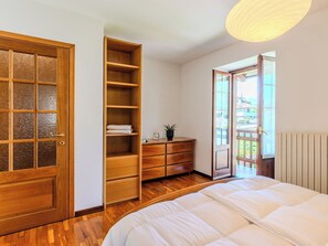 Ein Schlafzimmer mit Bett, Holzschrank, Schminktisch und Blick durch eine geöffnete Tür.