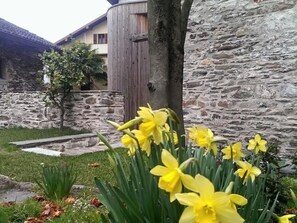 A stone building with a wooden post and daffodils in the foreground. - Corte delle Camelie - Wohnung im Erdgeschoss by Interhome (Vira)