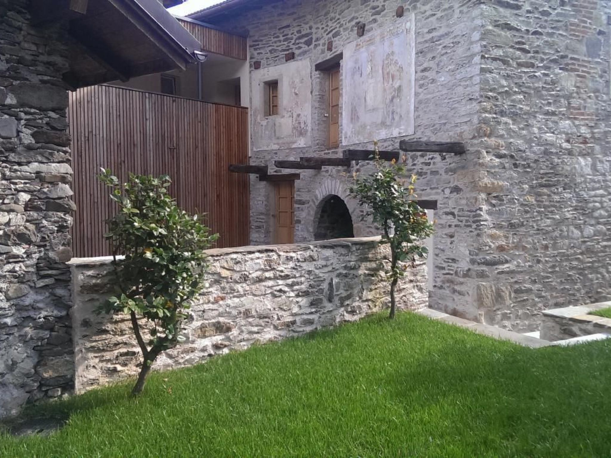 A stone building with a wooden balcony, a small arched window, and a grassy area in front.
