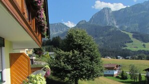 Hotel met een balkon versierd met bloemen, een verzorgd gazon en een uitzicht op bergen op de achtergrond.
