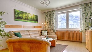 Een moderne woonkamer met een beige bank, een bijzettafeltje en een groot raam met gordijnen.