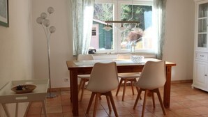 Uma área de refeições com uma mesa de madeira e quatro cadeiras, um vaso de flores e uma janela com cortinas.