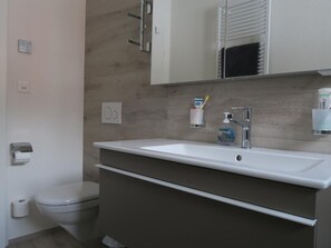 Een moderne badkamer met een wit wastafelmeubel, een donker kastje en een spiegel erboven.