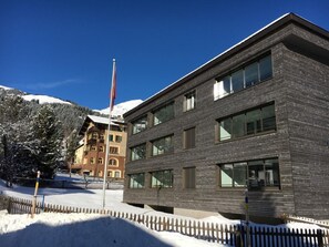 Een modern gebouw met grote ramen en een houten gevel, omgeven door sneeuw en een houten hek.
