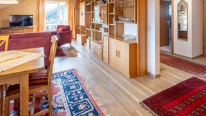 Ein gemütliches Wohnzimmer mit Holzbalkendecke, einer Couch, einem Esstisch und einem Bücherregal voller Bücher und Dekoration.