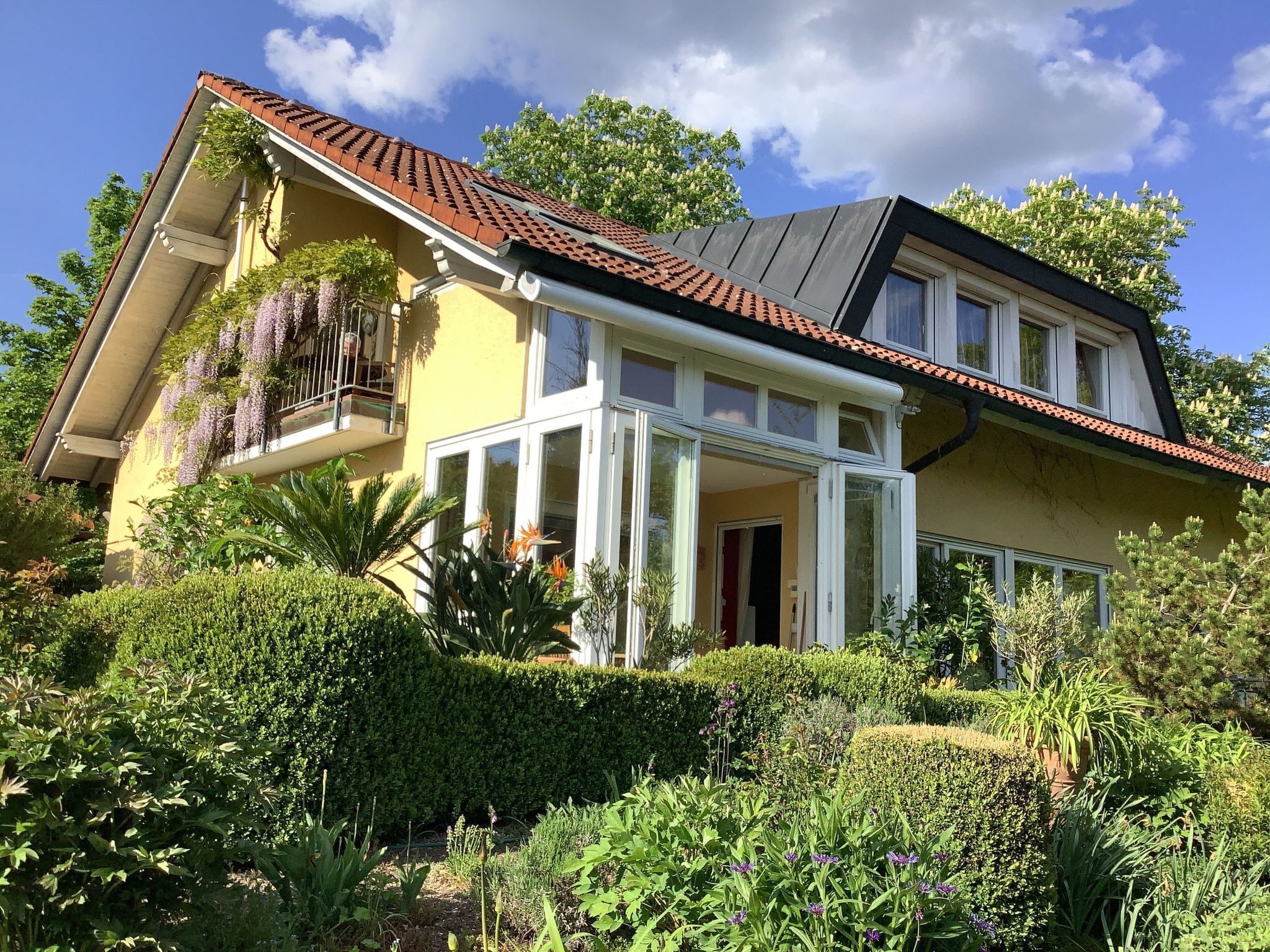 Een tweelaags huis met een balkon, omringd door weelderig groen en een verzorgde tuin.