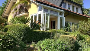 Ein zweistöckiges Haus mit Balkon, umgeben von üppigem Grün und einem gepflegten Garten.