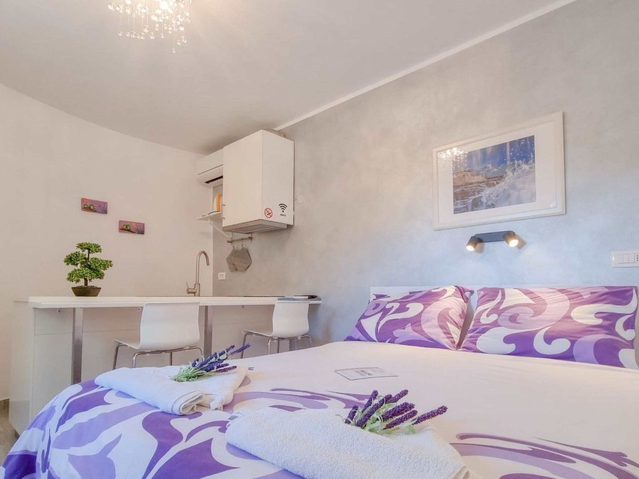Un dormitorio con una cama, un escritorio y una silla. Hay una planta pequeña en el escritorio y un cuadro en la pared.