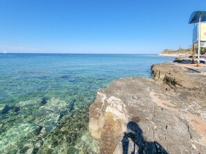 A rocky shoreline with clear water, a beach, and a signboard. - Gemütliches Studioappartement Silos Lavanda by Interhome (Buzinija)