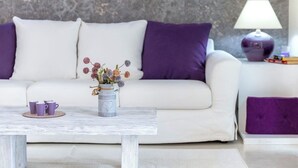 Un salon moderne avec un canapé blanc, des coussins violets, une table basse et un vase rempli de fleurs.