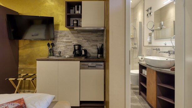 Quarto de hotel compacto com cozinha compacta, cama, televisão e banheiro com pia e espelho.