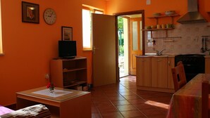 A compact kitchen with wooden cabinets, a stove, and a sink. There is a dining table with chairs and a small television on a stand. - Charmantes Ferienhaus in Bartići mit Terrasse by Interhome (Drenje)