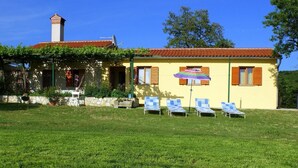 A yellow building with a red-tiled roof, a chimney, and a garden with blue lawn chairs and a striped umbrella. - Charmantes Ferienhaus in Bartići mit Terrasse by Interhome (Drenje)