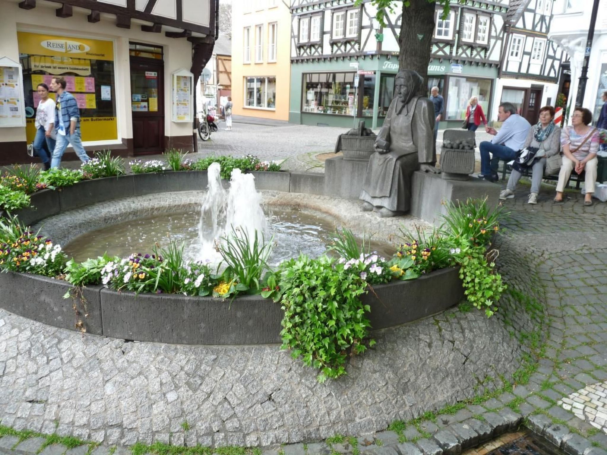 A public square with a circular fountain surrounded by flower beds and benches.