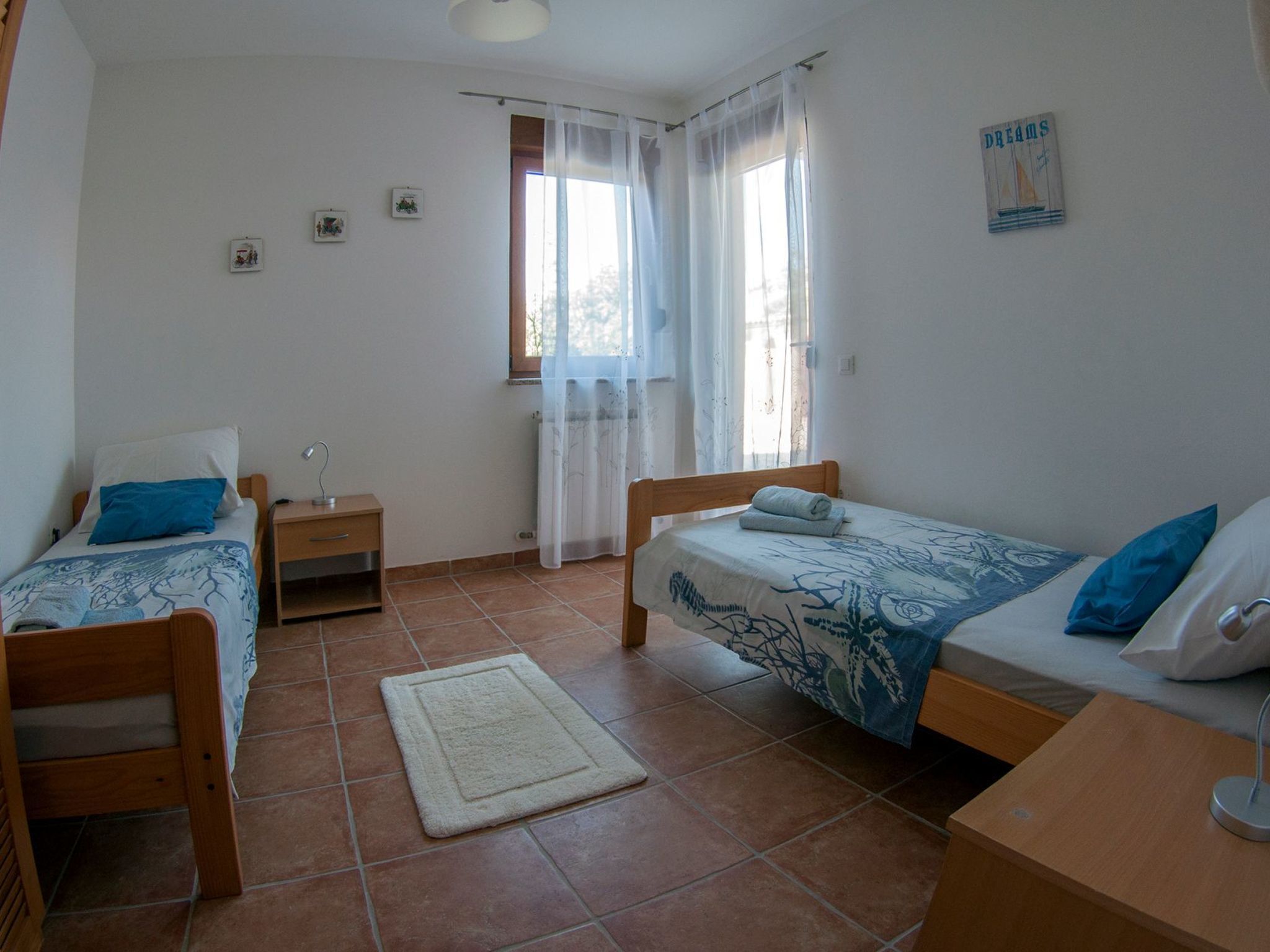 Un dormitorio con dos camas, una mesita de noche, un escritorio, una ventana con cortinas y una pequeña alfombra.