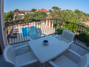 Ein Balkon mit einem weißen Tisch und Stühlen, ein Pool im Hintergrund und Blick auf Häuser und Bäume.