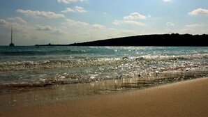 Ein Strand mit blauem Himmel, ruhigem Wasser und einem Segelboot in der Ferne.