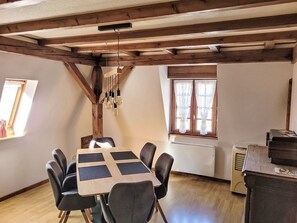 A dining area with a wooden table and chairs, a hanging light fixture, and a window with curtains. - Das Ferienhaus Caspar für 2 bis 4 Personen by Interhome (Obernai)