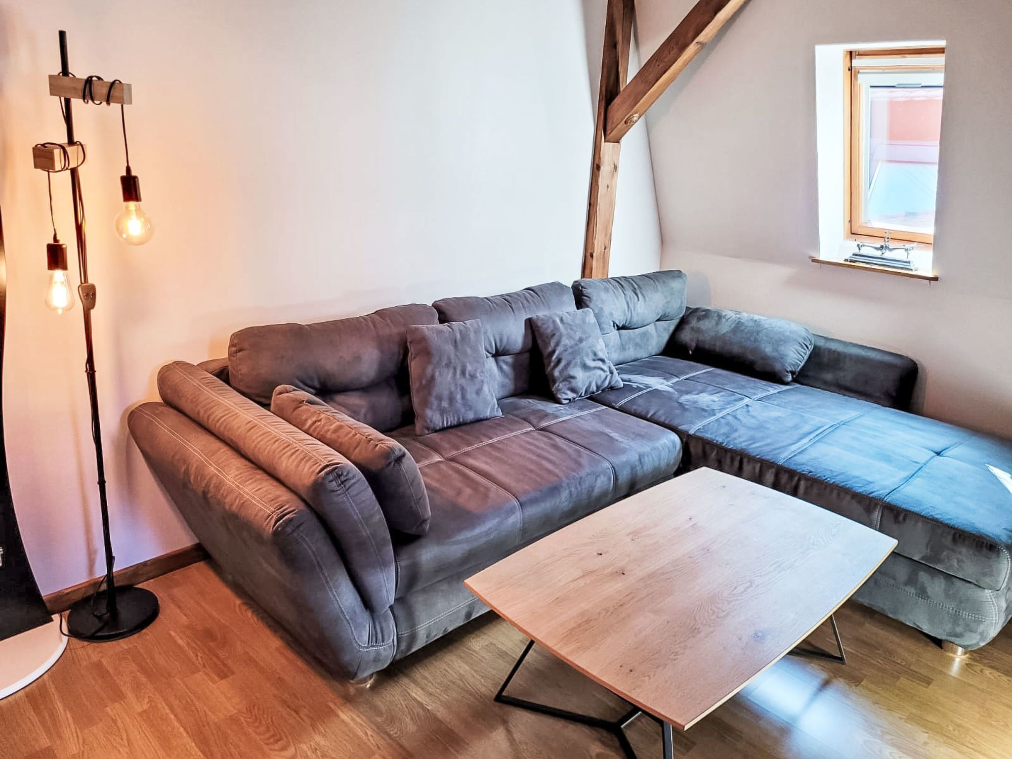 Un salon moderne avec un canapé d’angle, une table basse en bois et un lampadaire.