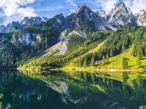 Un paisaje montañoso con un lago que refleja el entorno, rodeado de densos bosques y picos rocosos.