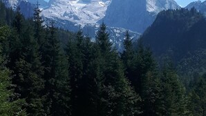 A mountainous landscape with dense forests and snow-capped peaks under a clear sky.