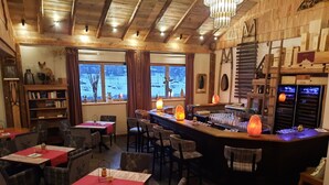 A cozy restaurant with wooden interiors, a bar area, and a view of a snowy landscape through large windows.