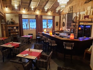Un restaurante acogedor con interiores de madera, una zona de bar y vistas a un paisaje nevado a través de amplios ventanales.