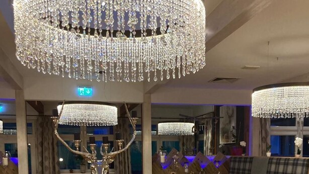 A restaurant interior with wooden flooring, round tables, and a large chandelier.