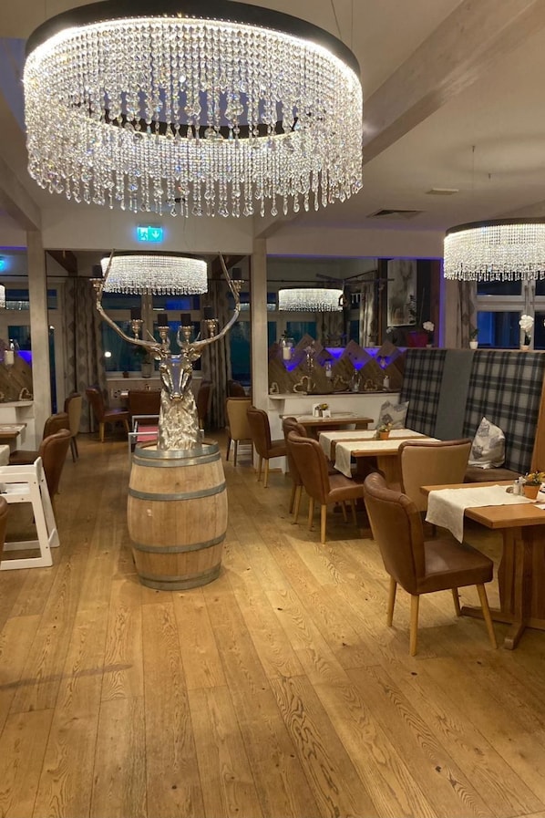 Interior de restaurante con suelo de madera, mesas redondas y una gran lámpara de araña.