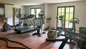 Een huisgymnasium met diverse fitnessapparaten, waaronder een loopband, een elliptische trainer en een hometrainer.