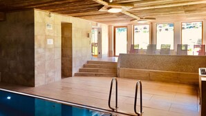 A pool area with a wooden ceiling, a reception desk, and a view of the outdoors through large windows. - Deluxapartment Simon by Interhome (Gosau)
