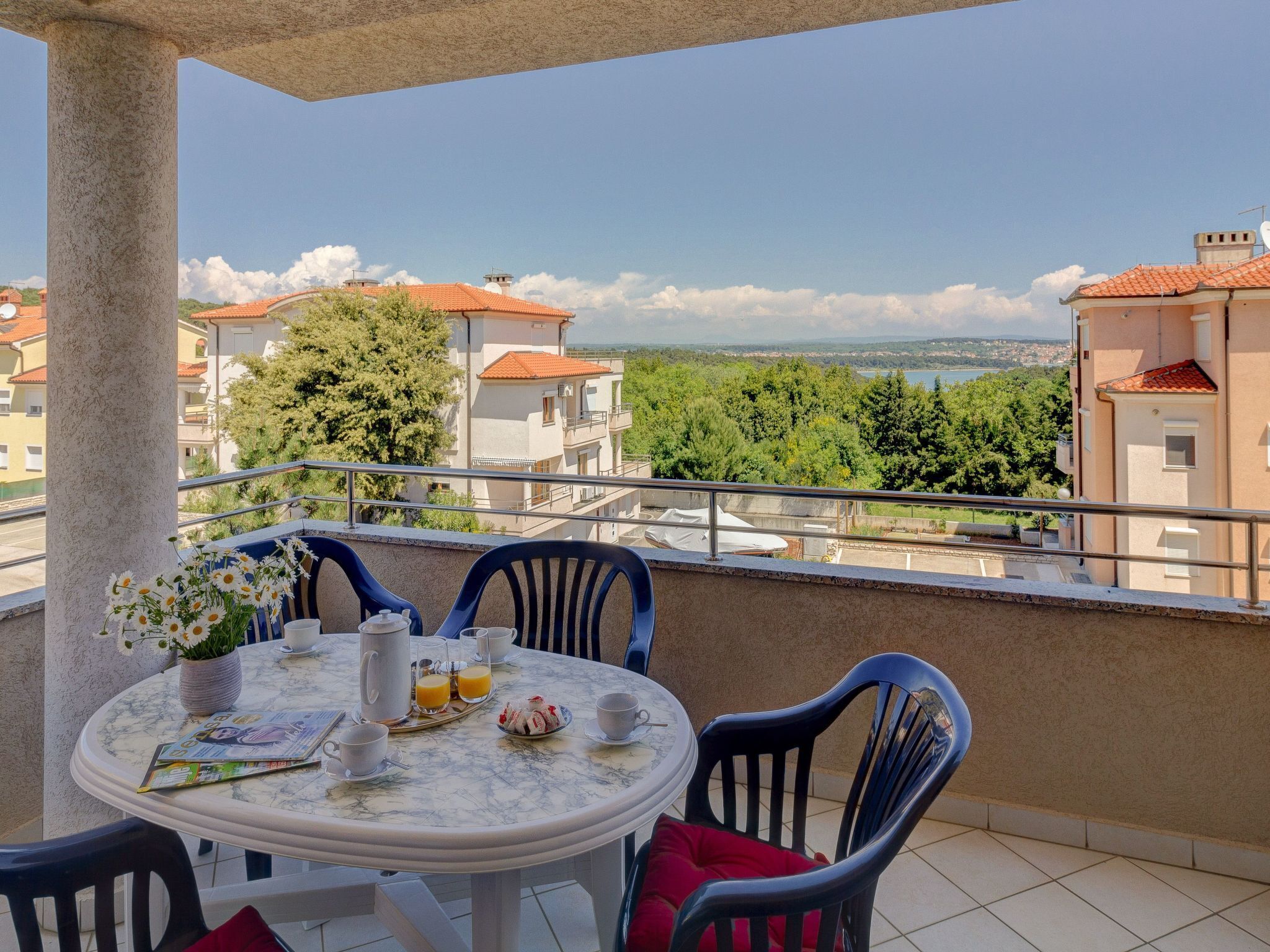 Varanda com mesa redonda posta para o café da manhã, com vista panorâmica para prédios e árvores.
