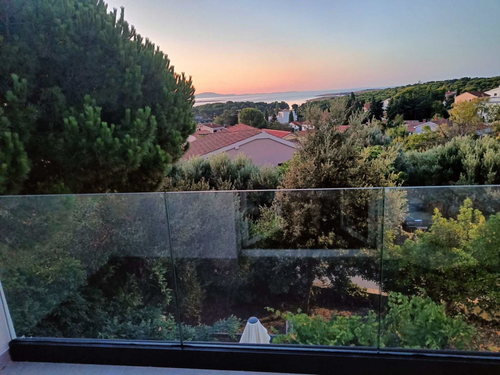 Ein Balkon mit Blick auf eine Küstenstadt, Bäume und einen Sonnenuntergang.