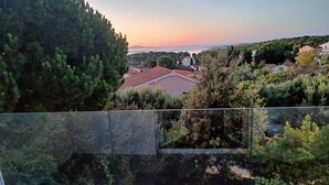A balcony with a view of a coastal town, trees, and a sunset.