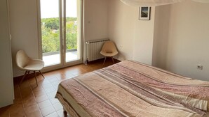 A bedroom with a bed, a ceiling fan, a window with a view, and a chair.
