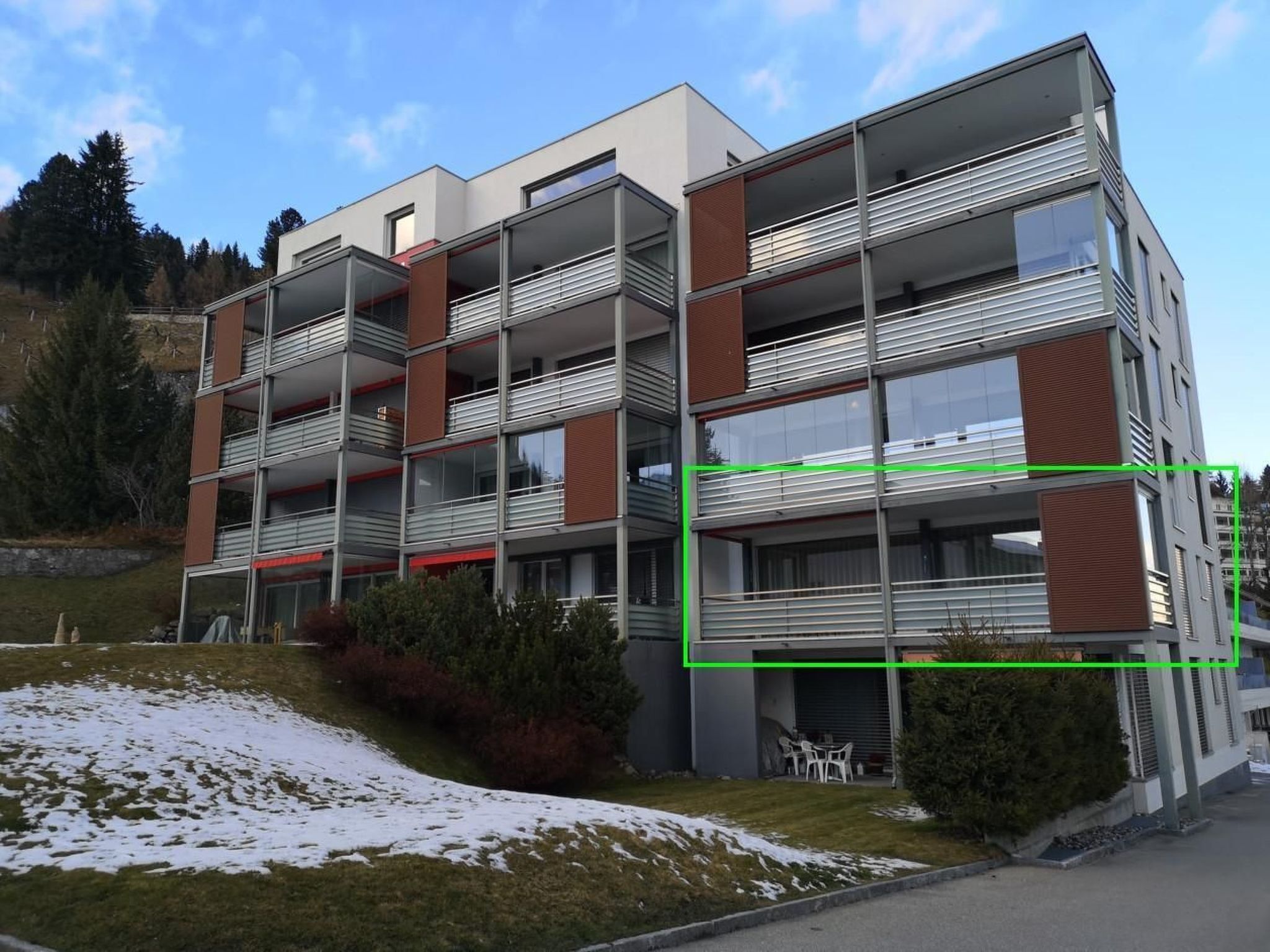 A multi-story building with balconies, a covered outdoor seating area, and a sloped roof.