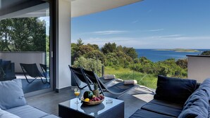 Uma área de estar moderna ao ar livre, com vista para o mar e vegetação.