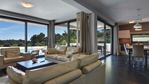 Uma sala de estar moderna com janelas amplas, um sofá, uma mesa de centro e uma área de jantar.