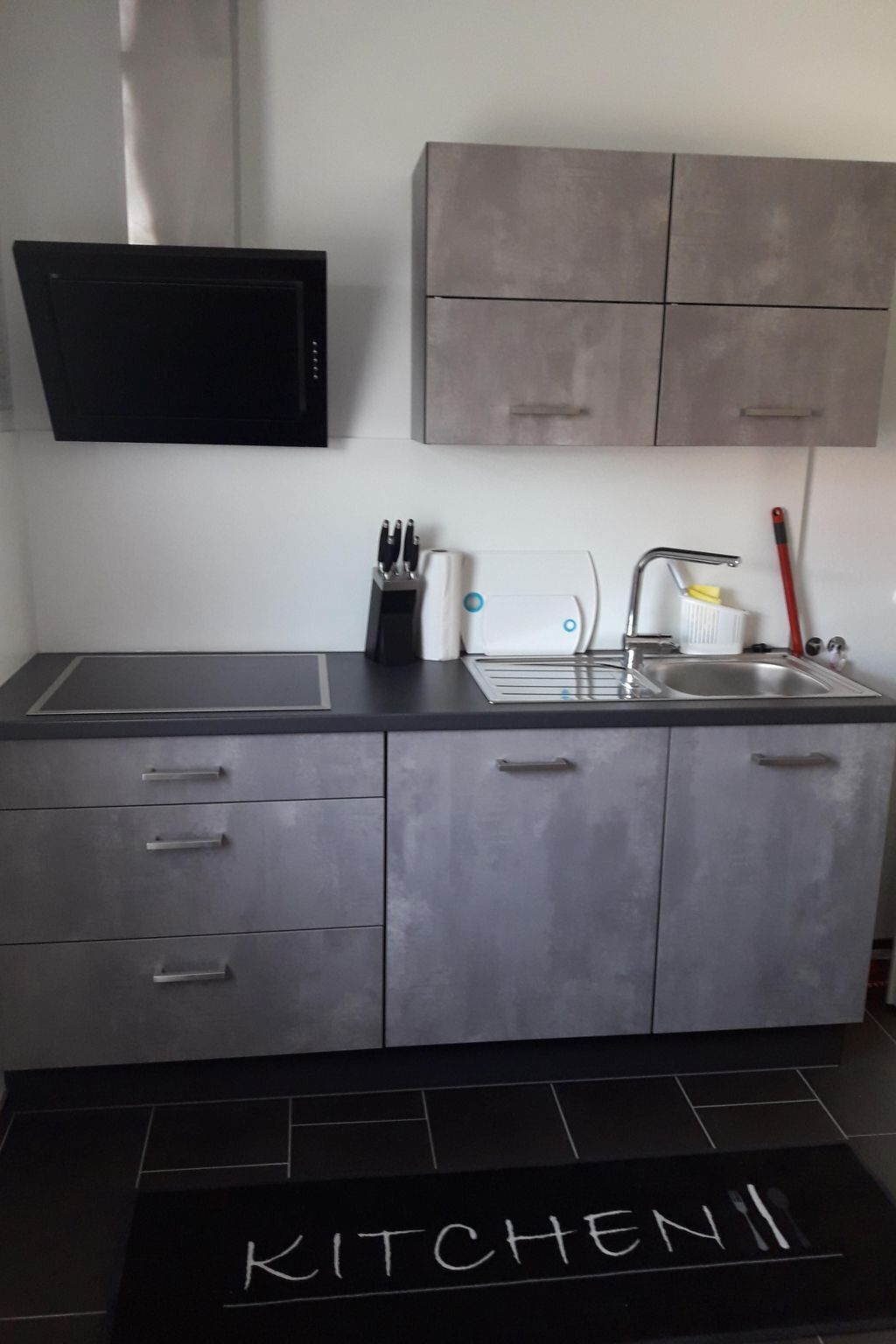 A modern kitchen with grey cabinets, a black countertop, a built-in microwave, a toaster, and a sink.