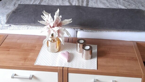 Ein ordentlich eingerichtetes Schlafzimmer mit einem hölzernen Kopfteil, einem Bett mit gemusterten Textilien und einem Nachttisch mit Dekoration.
