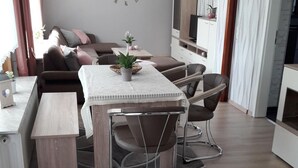Ein modernes Wohnzimmer mit Essbereich, mit Holzboden, einem Esstisch mit Stühlen, einer Couch und einer dekorativen Wanduhr.