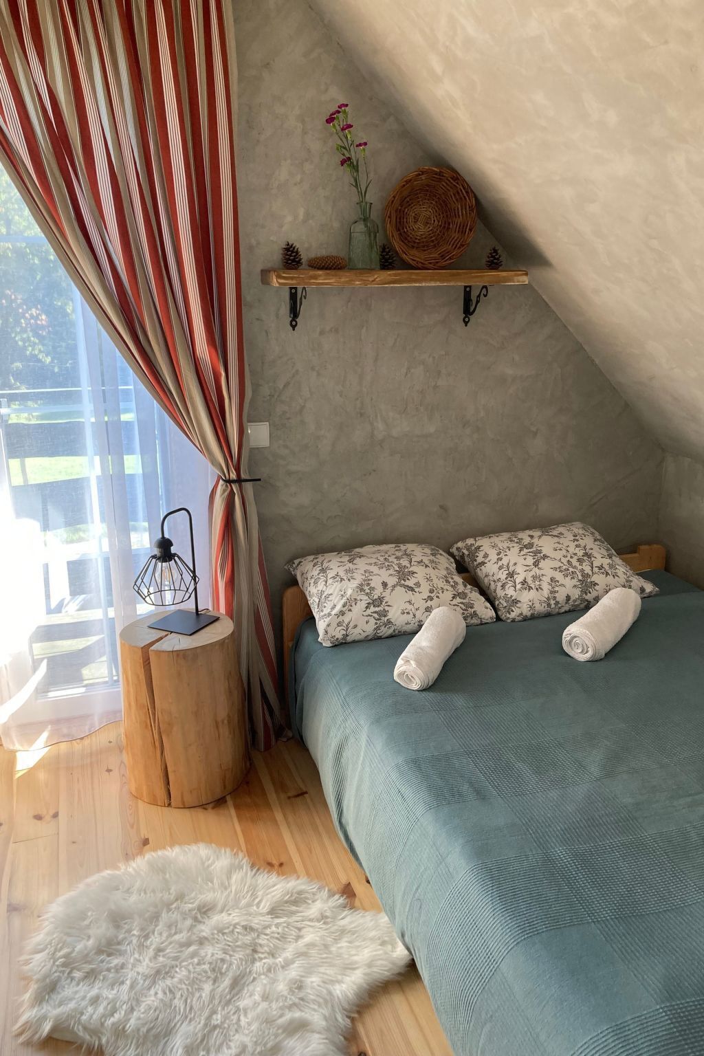 Une chambre confortable avec un lit, des oreillers, une petite table d’appoint en bois, un tapis moelleux et une fenêtre avec des rideaux.