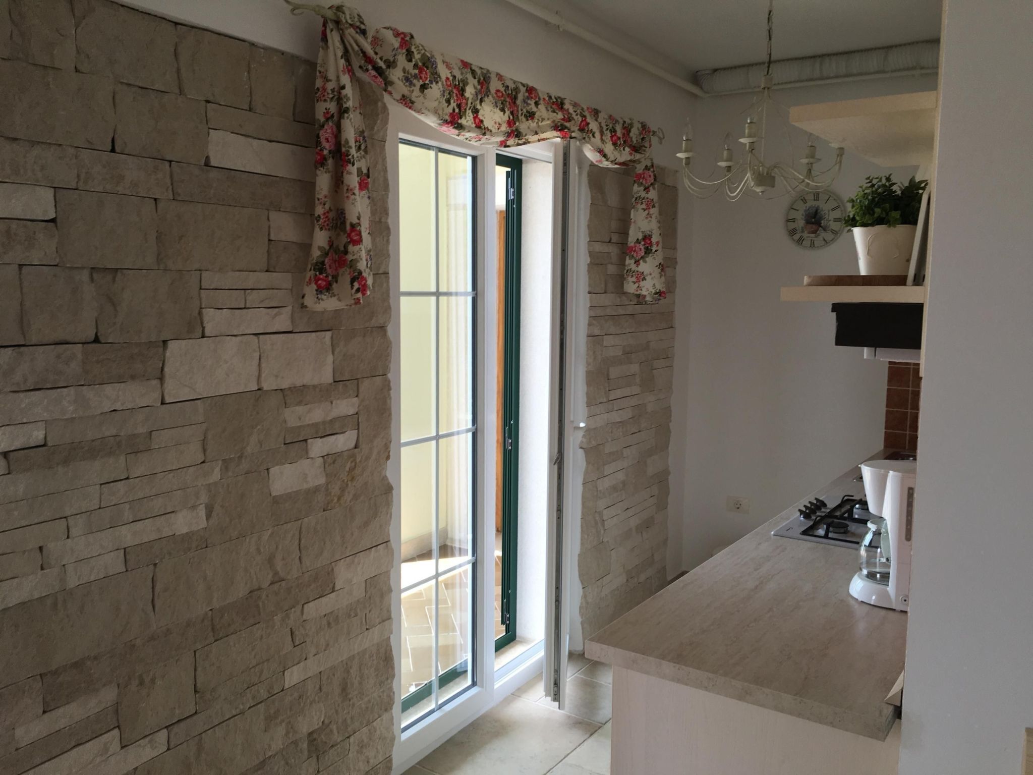 A kitchen with a stone wall, a sliding glass door, a chandelier, and a clock on the wall.